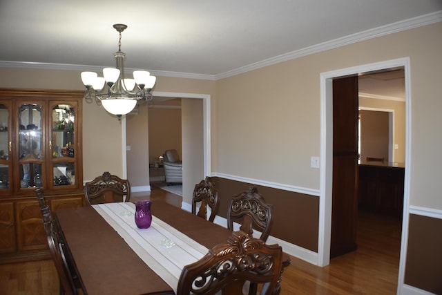 dining space featuring a notable chandelier, ornamental molding, baseboards, and wood finished floors