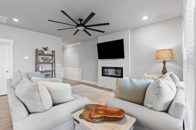 living room featuring ceiling fan, a large fireplace, and light wood-type flooring