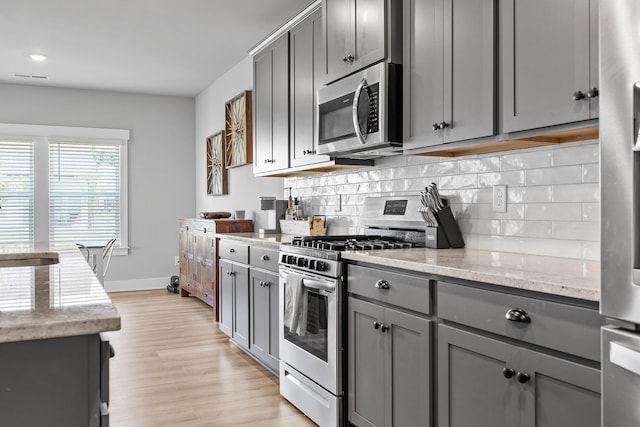 kitchen with light stone countertops, appliances with stainless steel finishes, light wood-type flooring, and gray cabinetry