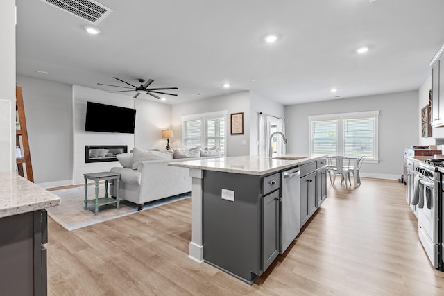 kitchen with a kitchen island with sink, sink, light stone countertops, and appliances with stainless steel finishes