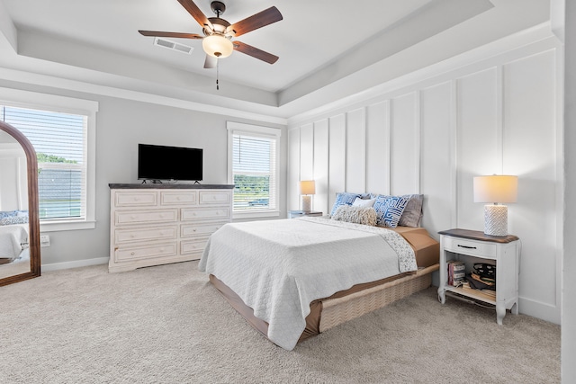 carpeted bedroom featuring multiple windows, a tray ceiling, and ceiling fan