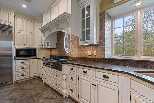 kitchen with backsplash, built in appliances, a wealth of natural light, and dark tile patterned flooring