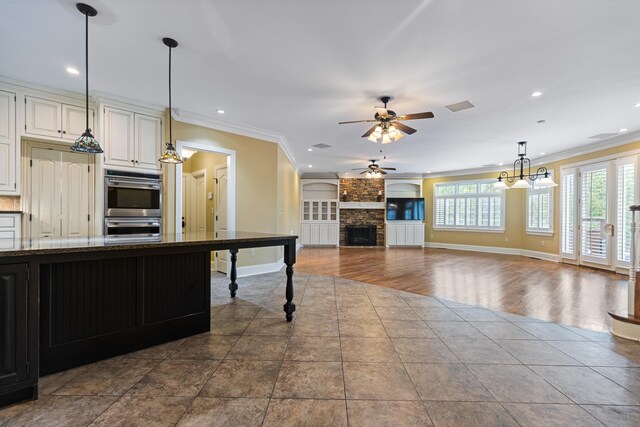 kitchen featuring crown molding, dark stone counters, ceiling fan with notable chandelier, and hardwood / wood-style flooring