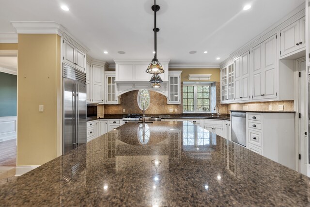 kitchen with built in appliances, decorative light fixtures, white cabinetry, and crown molding