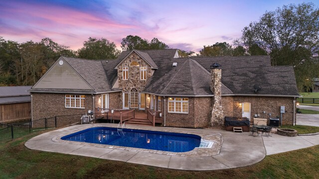 pool at dusk featuring a deck, central air condition unit, a fire pit, a patio area, and a hot tub