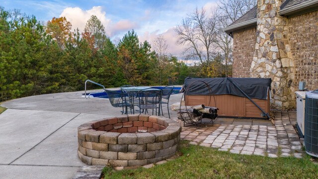 patio terrace at dusk featuring grilling area, a hot tub, and an outdoor fire pit