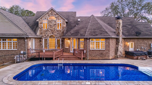 pool at dusk featuring a wooden deck and a hot tub