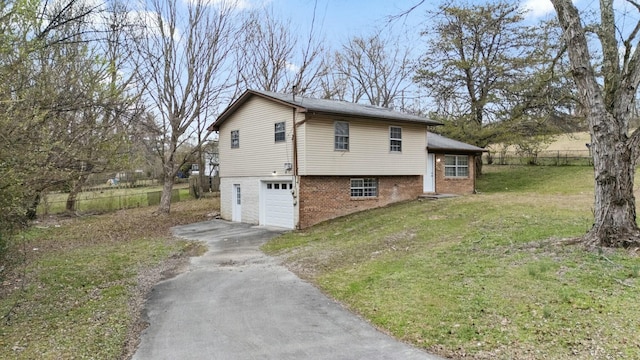 view of side of home featuring aphalt driveway, fence, a yard, an attached garage, and brick siding