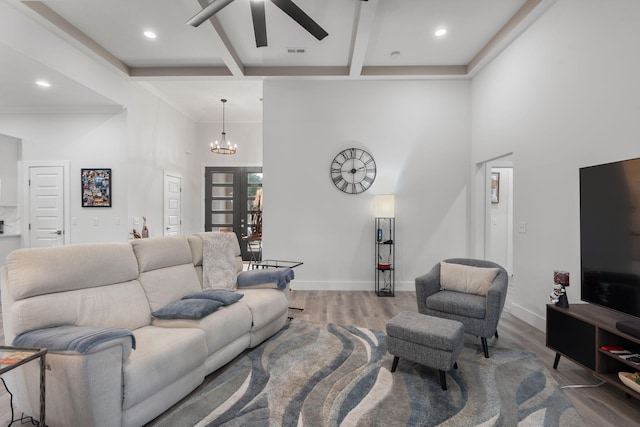 living room featuring hardwood / wood-style flooring, ceiling fan with notable chandelier, a towering ceiling, and beamed ceiling