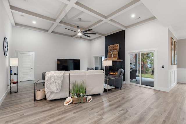 living room featuring light wood-type flooring, a large fireplace, ceiling fan, and coffered ceiling