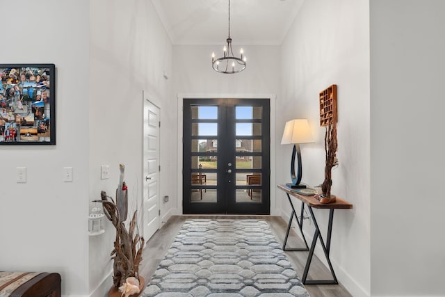 foyer entrance featuring a high ceiling, an inviting chandelier, french doors, hardwood / wood-style flooring, and ornamental molding