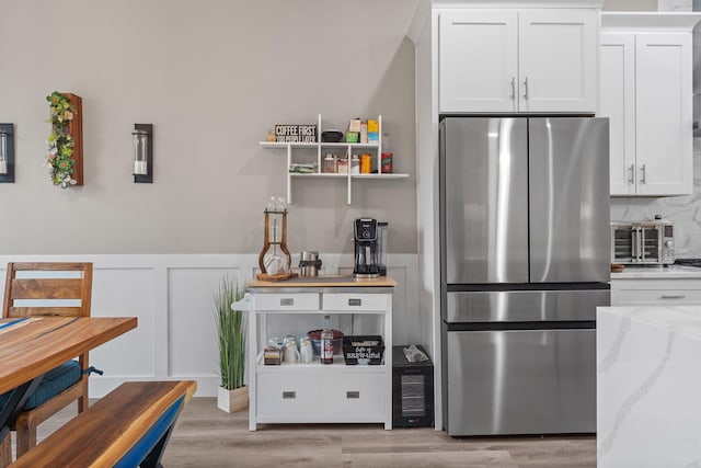 kitchen featuring light hardwood / wood-style flooring, white cabinetry, stainless steel refrigerator, and light stone counters