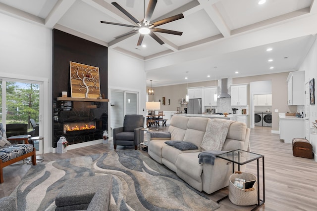 living room featuring beam ceiling, ceiling fan, a large fireplace, light hardwood / wood-style flooring, and independent washer and dryer