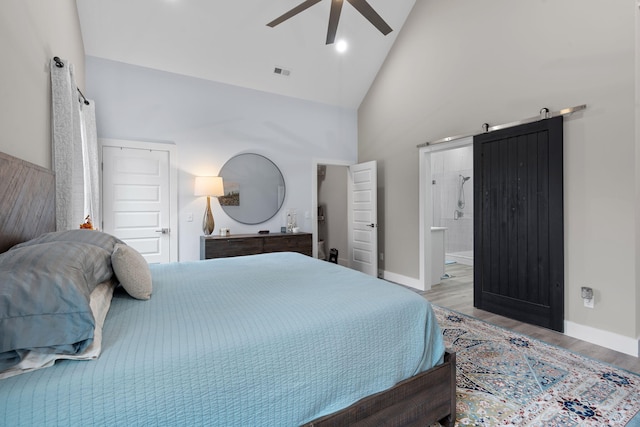 bedroom featuring ensuite bath, ceiling fan, a barn door, light hardwood / wood-style flooring, and high vaulted ceiling