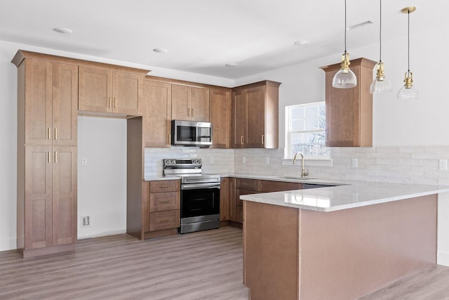 kitchen featuring decorative light fixtures, appliances with stainless steel finishes, brown cabinetry, a sink, and a peninsula
