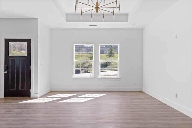 foyer entrance with a tray ceiling, visible vents, baseboards, and wood finished floors