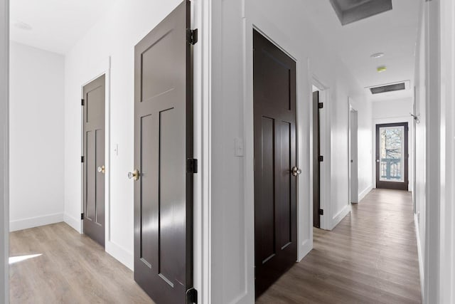 hall with light wood-type flooring, visible vents, and baseboards
