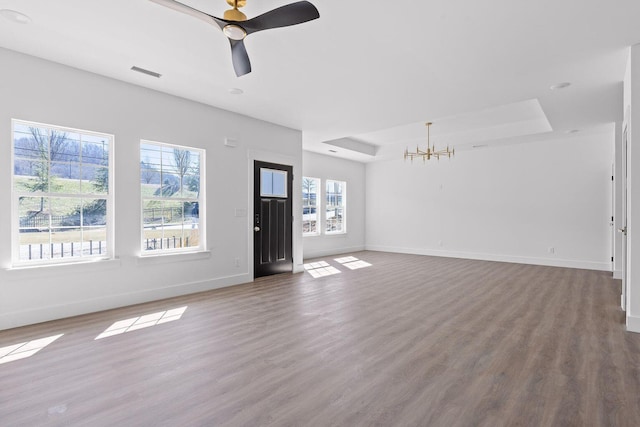 unfurnished living room with a tray ceiling, wood finished floors, visible vents, and baseboards