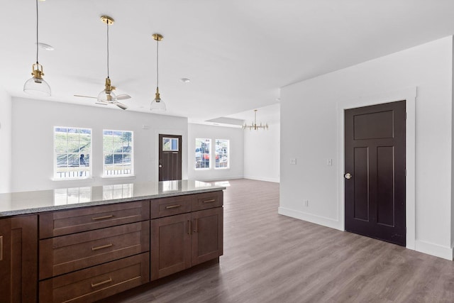 kitchen with wood finished floors, baseboards, open floor plan, hanging light fixtures, and light stone countertops