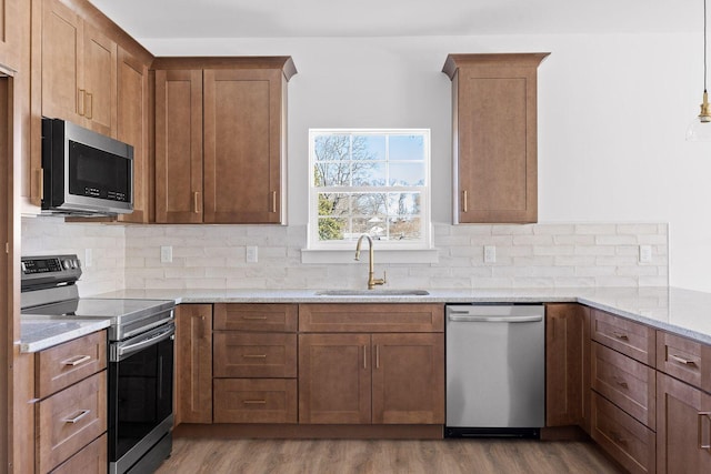 kitchen featuring light stone counters, stainless steel appliances, wood finished floors, a sink, and brown cabinets
