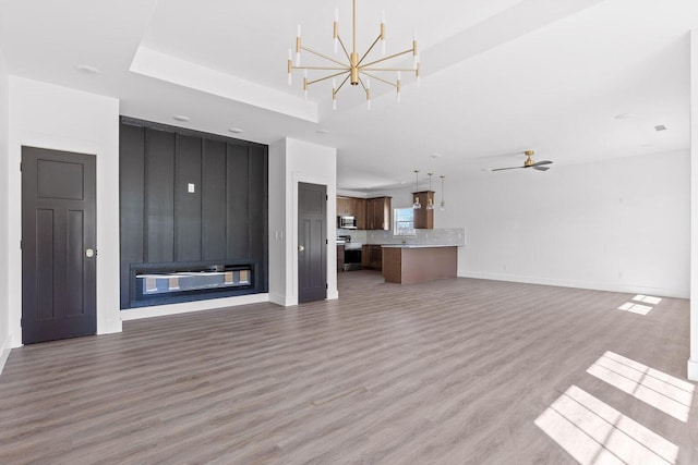 unfurnished living room with light wood-type flooring, a fireplace, baseboards, and ceiling fan with notable chandelier