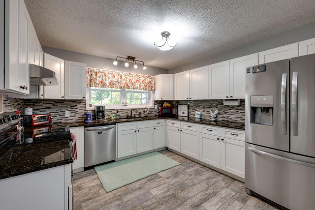 kitchen featuring dark stone counters, light wood-type flooring, a textured ceiling, appliances with stainless steel finishes, and white cabinetry