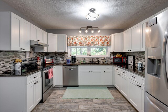 kitchen with appliances with stainless steel finishes, backsplash, dark stone counters, sink, and white cabinets