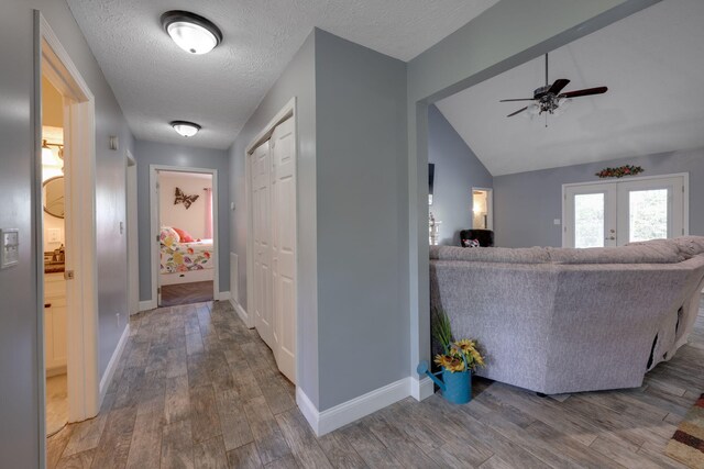 corridor featuring a textured ceiling, french doors, vaulted ceiling, and hardwood / wood-style flooring