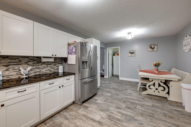 kitchen with a textured ceiling, white cabinets, dark stone counters, and stainless steel refrigerator with ice dispenser