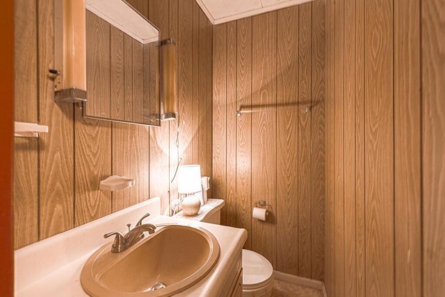 half bath with wooden walls, toilet, and a sink