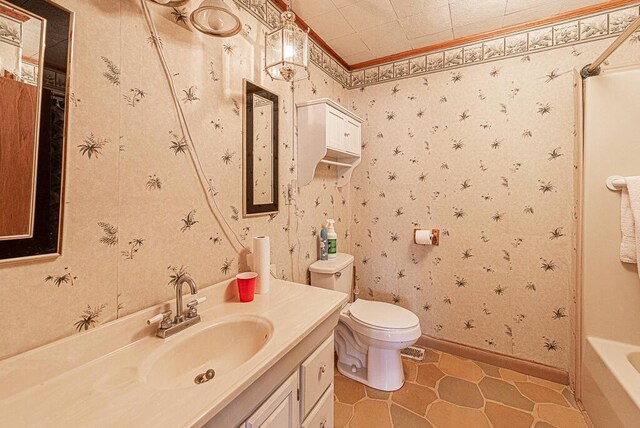 bathroom featuring vanity, baseboards, wallpapered walls, ornamental molding, and toilet