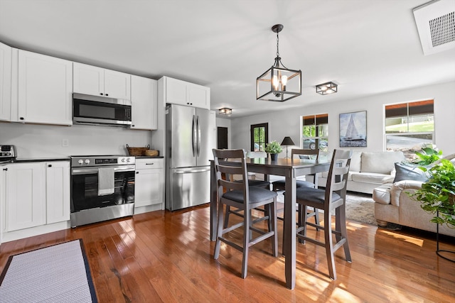 kitchen featuring white cabinets, dark countertops, appliances with stainless steel finishes, hardwood / wood-style floors, and open floor plan