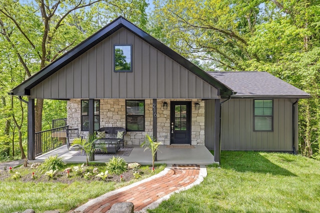 view of front facade with covered porch, a front yard, board and batten siding, and stone siding