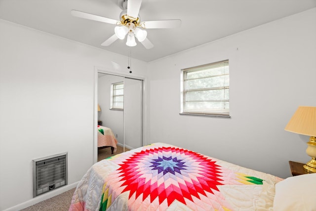 carpeted bedroom with heating unit, ceiling fan, and a closet