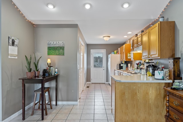kitchen with light countertops, a peninsula, under cabinet range hood, light tile patterned floors, and freestanding refrigerator
