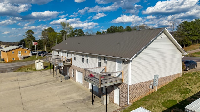 rear view of property with a wooden deck, driveway, an attached garage, and metal roof