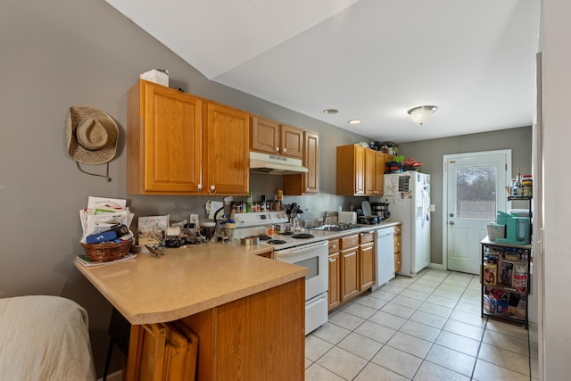 kitchen with light countertops, a peninsula, white appliances, under cabinet range hood, and a sink