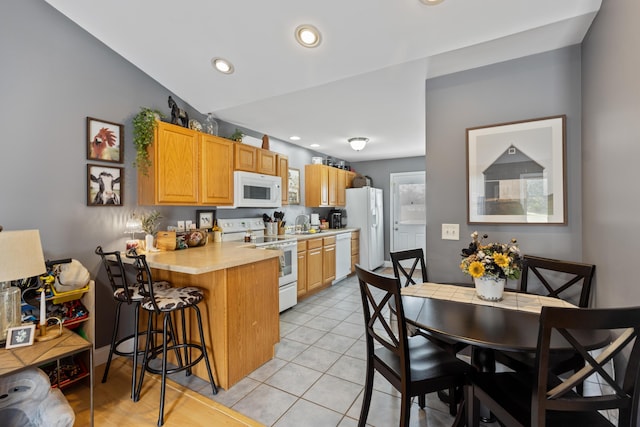 kitchen with light countertops, a peninsula, white appliances, a breakfast bar area, and light tile patterned floors
