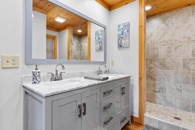 bathroom with a tile shower, wooden ceiling, double vanity, and a sink