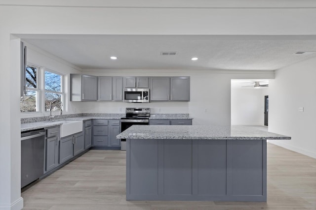 kitchen featuring a sink, gray cabinets, visible vents, light stone counters, and appliances with stainless steel finishes