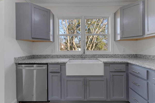 interior space featuring gray cabinets, stainless steel dishwasher, light stone countertops, and a sink