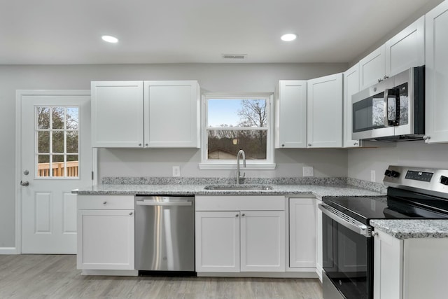 kitchen featuring white cabinets, appliances with stainless steel finishes, light stone counters, and sink