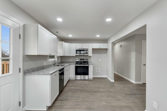 kitchen featuring white cabinets, sink, light hardwood / wood-style flooring, light stone countertops, and stainless steel appliances