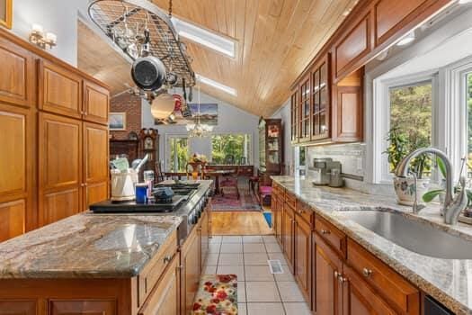 kitchen with sink, light hardwood / wood-style flooring, vaulted ceiling with skylight, a kitchen island, and light stone counters