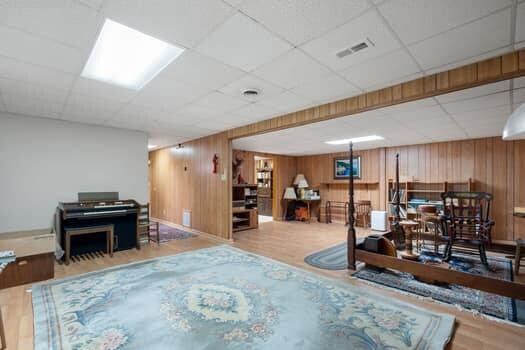 living room featuring hardwood / wood-style floors, a paneled ceiling, and wooden walls