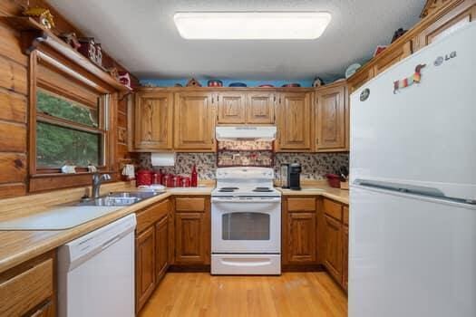 kitchen with backsplash, sink, white appliances, and light hardwood / wood-style flooring