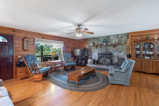 living room featuring a stone fireplace, wood walls, ceiling fan, and hardwood / wood-style flooring