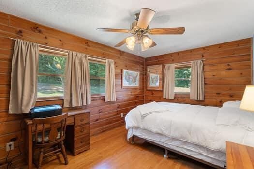 bedroom with multiple windows, ceiling fan, wood walls, and light wood-type flooring