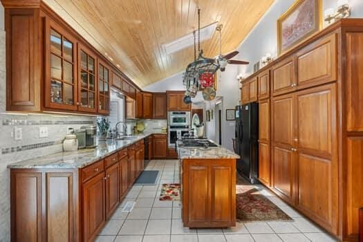 kitchen with light tile patterned flooring, lofted ceiling, a kitchen island, wood ceiling, and stainless steel appliances