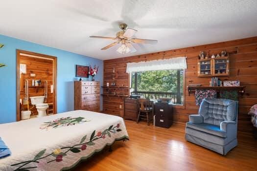 bedroom with hardwood / wood-style flooring, ceiling fan, wooden walls, and connected bathroom